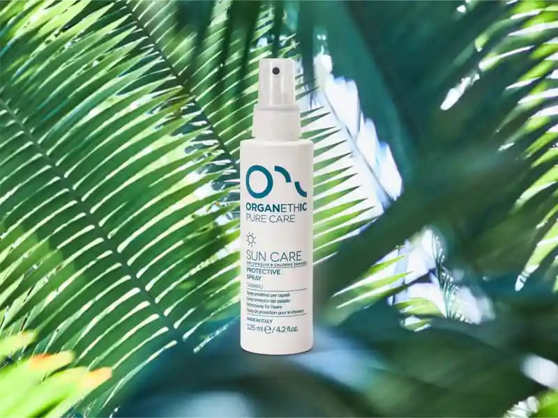 A bottle of sun care protective hair spray standing on a palm leaf.
