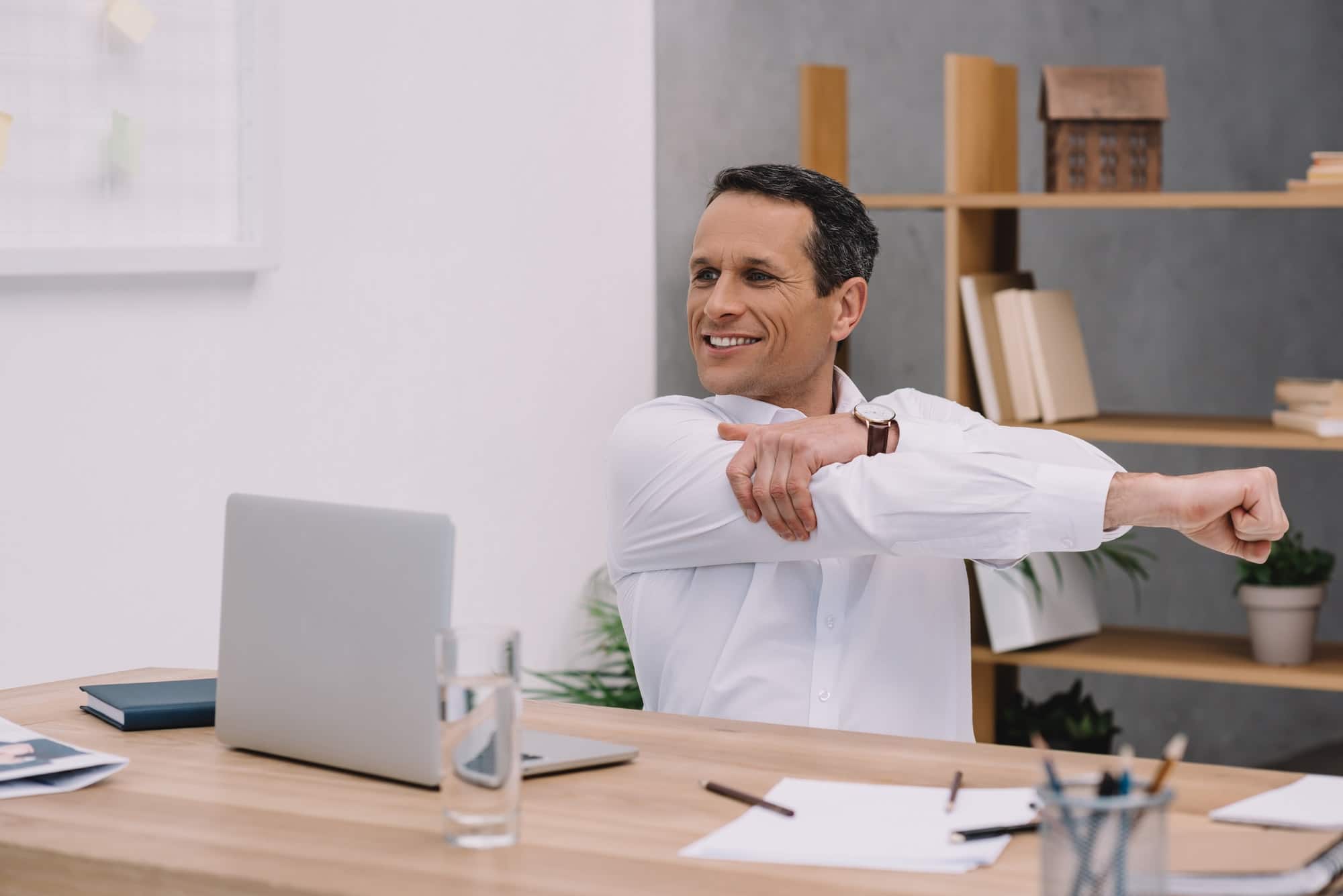 happy mature businessman warming up his shoulder while working at office