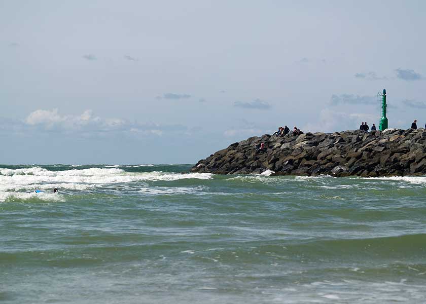 Sydmolen i Hvide Sande på en dejlig sommerdag, surferen i vandet prøver at fange den næste bølge
