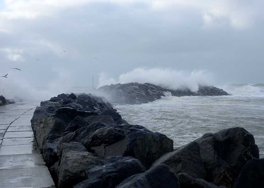 Bølger slår ind over molerne ved Hvide Sande på en meget blæsende dag, fyret er helt dækket i vand