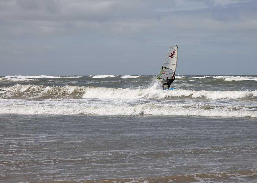 Vindsurferen har netop fået vind i sejlene og styr mod bølgerne længere fra kysten.