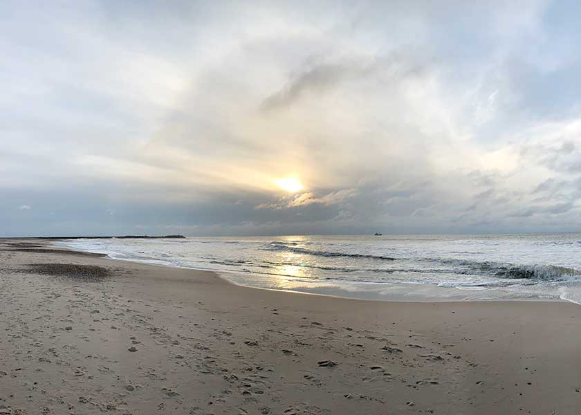 Den nedgående sol ved molerne i Hvide Sande bliver næsten opslugt a f de tunge grå skyer som hænger lavet over havet