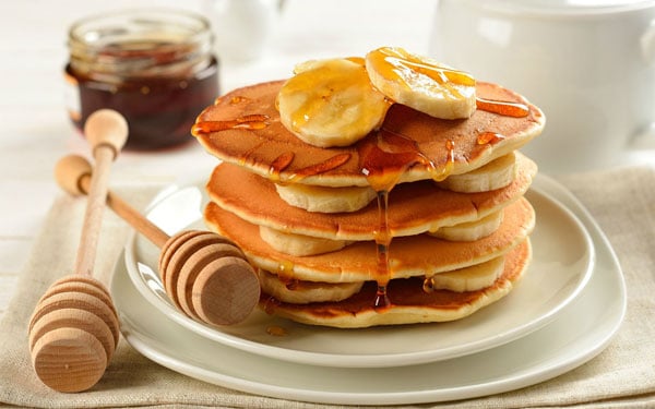 A stack of pancakes with honey and bananas, a forgiving combination of good food.