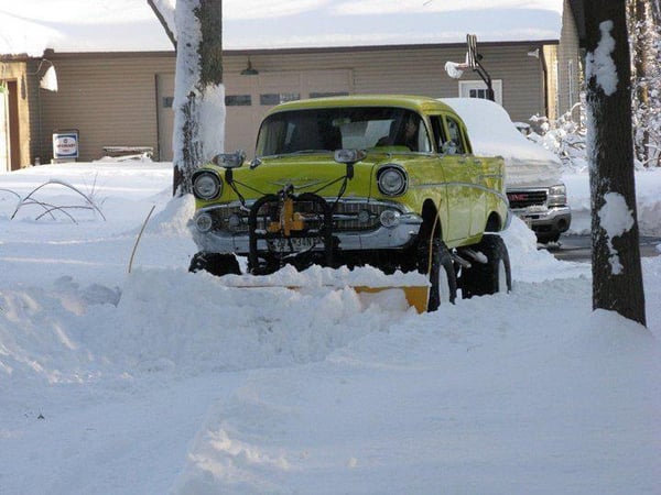 A yellow car plows snow in front of a house, showcasing just cool ass cars.