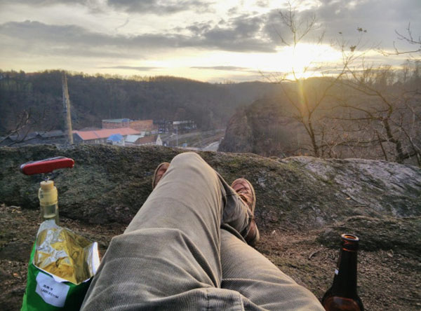 A person indulging in weekend confessions, sitting on a rock with a bottle of wine and a bottle of beer.