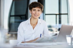 Een glimlachende zakenvrouw die als softwareontwikkelaar aan een bureau zit met een laptop.