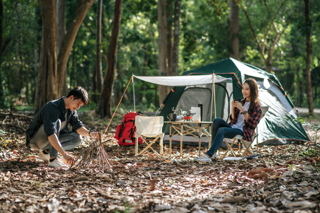 Young mand picking branches and put them together, He preparing preparing a pile of firewood for fire camping on night and pretty girl friend sitting at front of camping tent