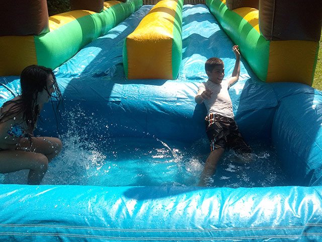Kids splashing into the pool of the slip n' Slide pool rental